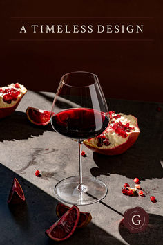 a glass of red wine sitting on top of a table next to some sliced pomegranate