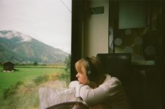 a woman sitting on a train with headphones in her ears looking out the window