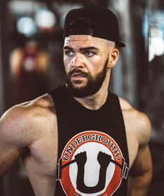 a man with a beard wearing a black tank top and standing in front of a gym machine