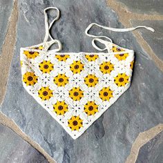 a crocheted sunflower bib hanging on a stone floor with white string