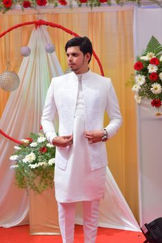 a man in a white suit and tie standing next to a red carpet with flowers on it