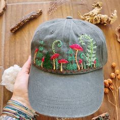 a person holding up a hat with embroidered mushrooms on it and other items surrounding it