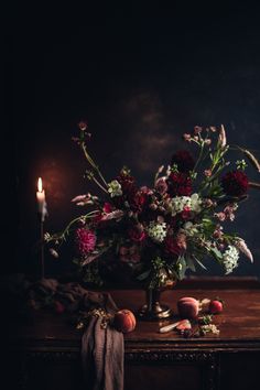 a bouquet of flowers sitting on top of a wooden table next to a lit candle