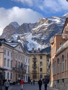 people are walking down the street in front of some buildings and mountains with snow on them