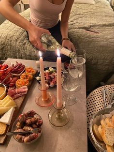 a woman pours wine from a bottle in front of a tray of food on a bed