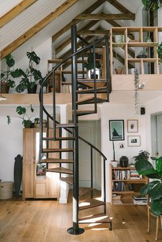 there is a spiral staircase in the middle of this living room with wood floors and white walls