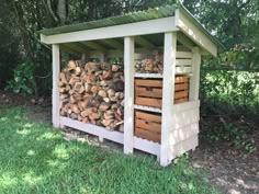 a shed with logs stacked on top of it in the grass next to some trees