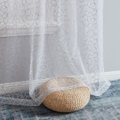 a basket sitting on the floor in front of a sheer curtain