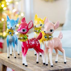 four little deer figurines are sitting on a wooden table in front of a christmas tree