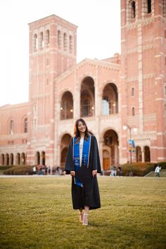 a woman standing in front of a building wearing a graduation gown and holding a tassel