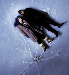 two people are laying on the snow with their arms around each other and looking at the camera