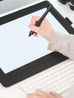 a person holding a pen and writing on a tablet screen with a keyboard next to it