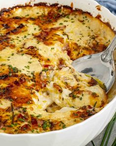 a close up of a casserole in a white dish with a serving spoon