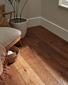 a wooden floor in a living room with a chair and potted plant next to it