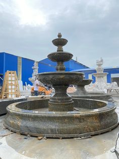 an outdoor fountain in front of a blue building with workers working on the back wall