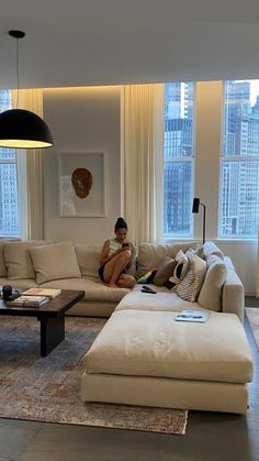 a woman sitting on a couch in a living room next to a window with large windows