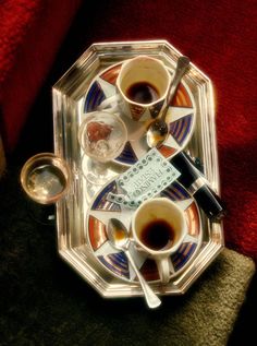 two cups of coffee sit on a tray with spoons and silverware in it