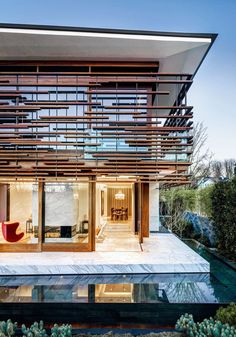 a modern house with glass walls and wooden slats on the roof, overlooking a pool