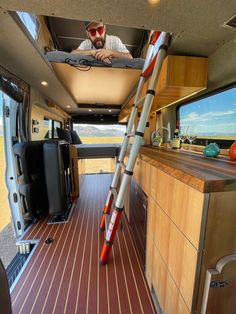 a man sitting in the back of a van looking at something on the floor and ladder