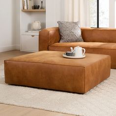 a brown leather couch and ottoman in a living room with white rugs on the floor