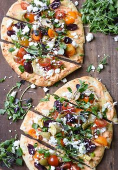 two flatbread pizzas topped with fresh vegetables and feta cheese on a wooden table