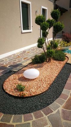 an outdoor area with gravel, rocks and trees in the center is shown here there is a stone path that leads to a small tree on one side of the house