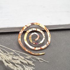 This handmade copper spiral scarf pin features a colorful patina which is different on each pin made. Some patina pins will have a rainbow of color while others will have a nice array of earthy colors. I have hammered a nice texture in the copper to bring out the highlights of color. This spiral pin works well with loosely knit scarves and knits. I enjoy translating my jewelry designs into shawl pins and seeing the possibilities. This pin measures approximately 1.75-2" in diameter.  This pin will arrive in a eco-friendly packaged kraft brown box with a ribbon. You may add gift wrap at checkout and have your gift beautiful wrapped in handmade eco-friendly paper. See All Spiral Jewelry In My Shop: https://www.etsy.com/shop/mymusejewelry?ref=seller-platform-mcnav&sort_order=date_desc&search_q Celtic Shawl, Spiral Jewelry, Sweater Pin, Hand Knit Sweater, Shawl Pin, Scarf Pin, Steamboat Springs, Jewelry Brooch, Knit Scarves