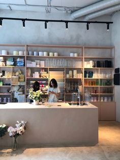 a woman standing in front of a counter with vases and flowers on the shelves