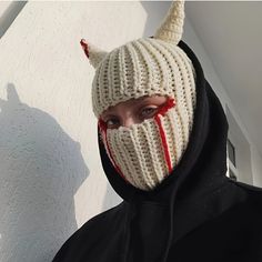 a person wearing a knitted mask with horns and fangs on their face is standing in front of a white wall