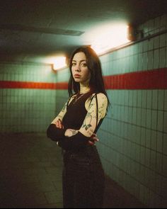 a woman standing in a subway station with her arms crossed and looking at the camera