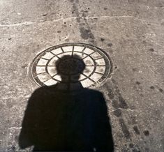 the shadow of a person standing in front of a manhole cover on a sidewalk