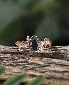 a black diamond ring sitting on top of a piece of wood with greenery in the background