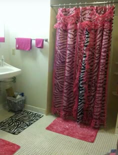 a zebra print shower curtain in a bathroom with pink rugs and towels on the floor