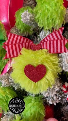 a green and red teddy bear with a heart on it's head next to christmas decorations