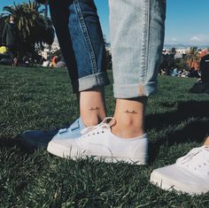 two people standing in the grass with their feet crossed and one has a small tattoo on her left ankle