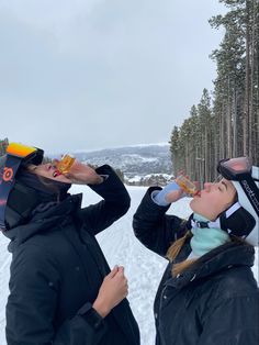 two people standing in the snow drinking from their bottles and looking up into the sky