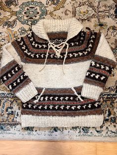 a white sweater with brown and black designs on it sitting on top of a rug