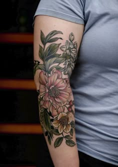 a woman's arm with flowers and leaves tattooed on her left arm, in grey shirt