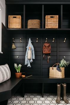 a black bench with baskets and coats hanging on the wall next to it is an entryway