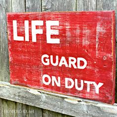 a red sign that says life guard on duty mounted to a wooden fence with the words,