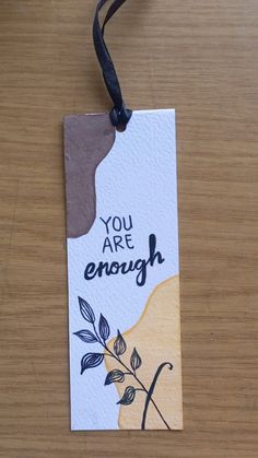 a tag that says you are enough on it with a flower and leaves design hanging from a black cord