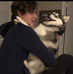 a woman sitting on top of a bed holding a dog in her lap and laughing