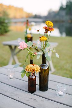 two brown bottles with flowers in them sitting on a picnic table next to some water