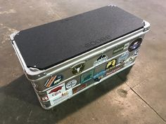 an aluminum case with various stickers on the inside and outside of it, sitting on concrete flooring