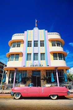 an old pink car is parked in front of a colorful building on the side of the road