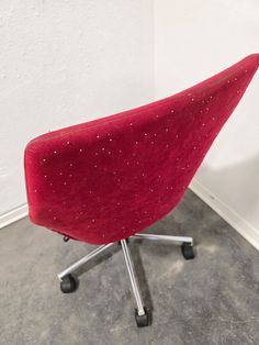 a red office chair sitting on top of a gray floor next to a white wall