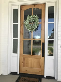 a wooden door with a wreath on the front and side glass doors, in front of a white brick house