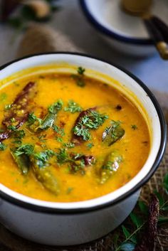 a white bowl filled with yellow soup and garnished with green leaves on top