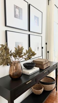 a black table topped with two vases filled with flowers and plants next to pictures on the wall