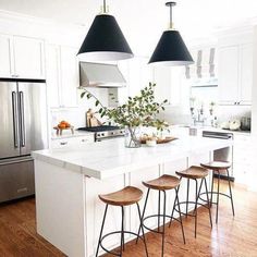 a kitchen island with four stools in front of it and three lights hanging from the ceiling